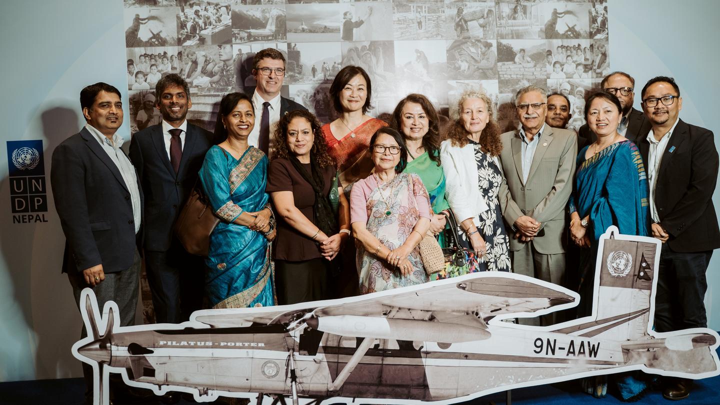 Group of formally dressed people posing beside a vintage propeller airplane model.
