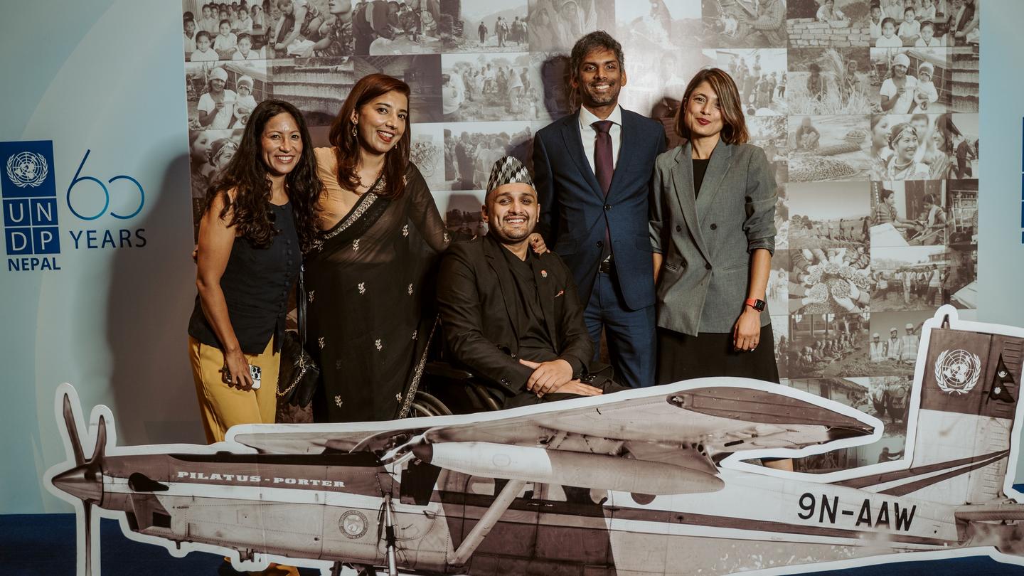 Group photo of people posing beside a small vintage airplane display at an aviation anniversary.