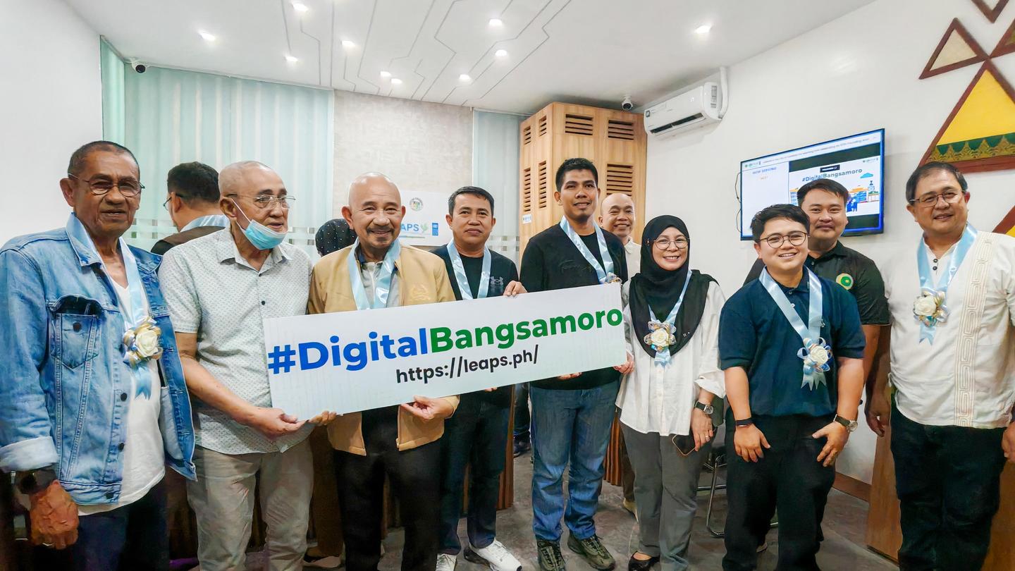 Diverse group posing while holding a banner that reads #DigitalBangsamoro in a bright office.