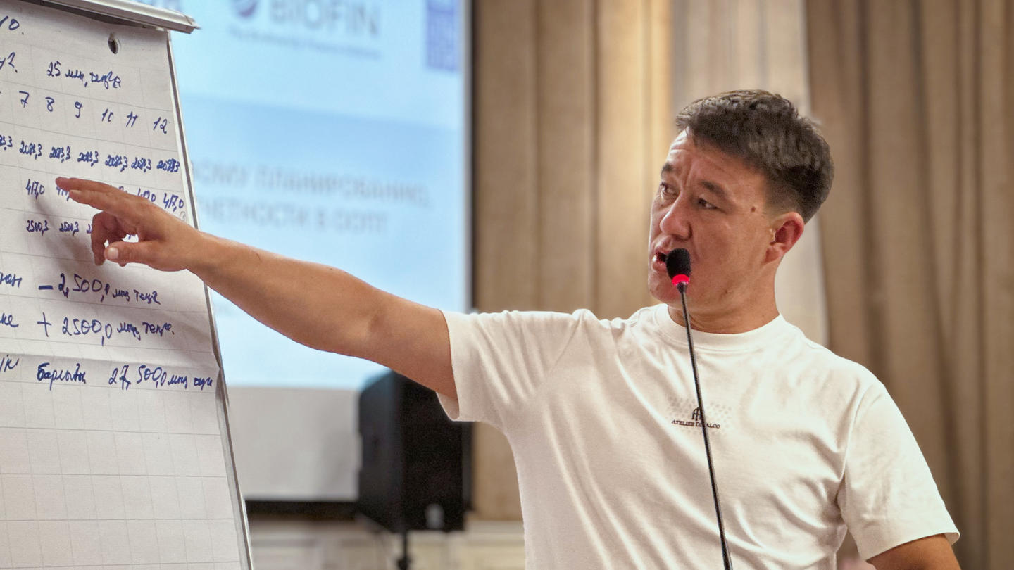 Man in a white shirt points at a flip chart during a presentation.