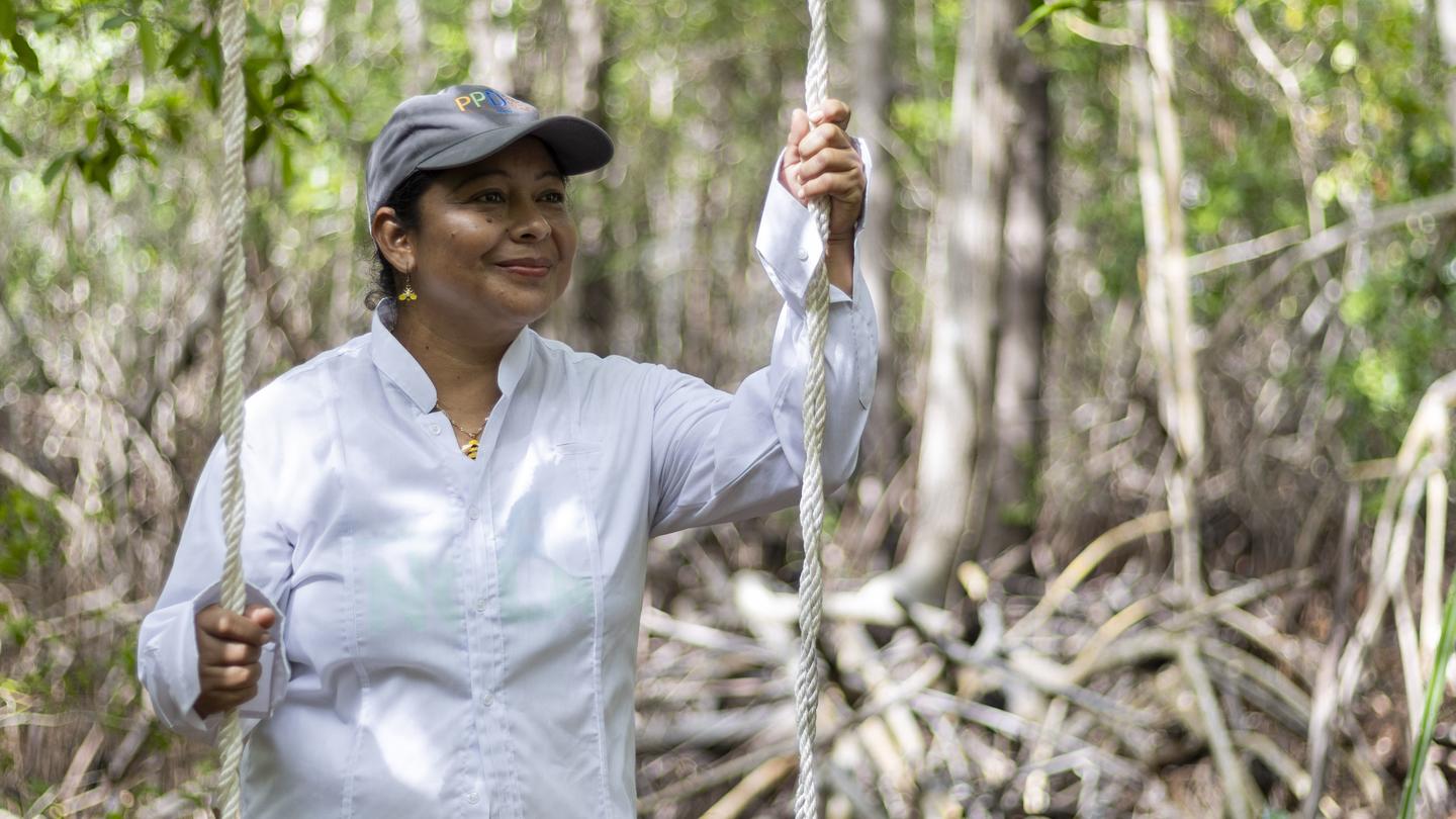 Smiling woman in a light shirt and cap grips vines in a forest.