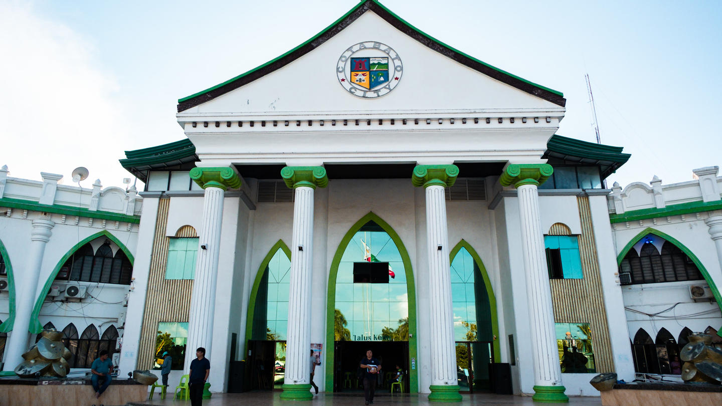 White and green neoclassical building with columns and arches, people gathered at the entrance.