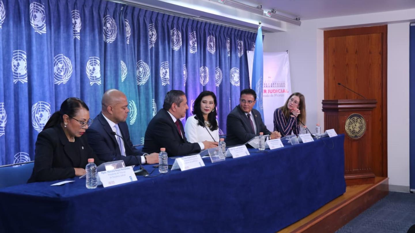 Panelists seated at a long blue-draped table on stage, blue curtain backdrop.