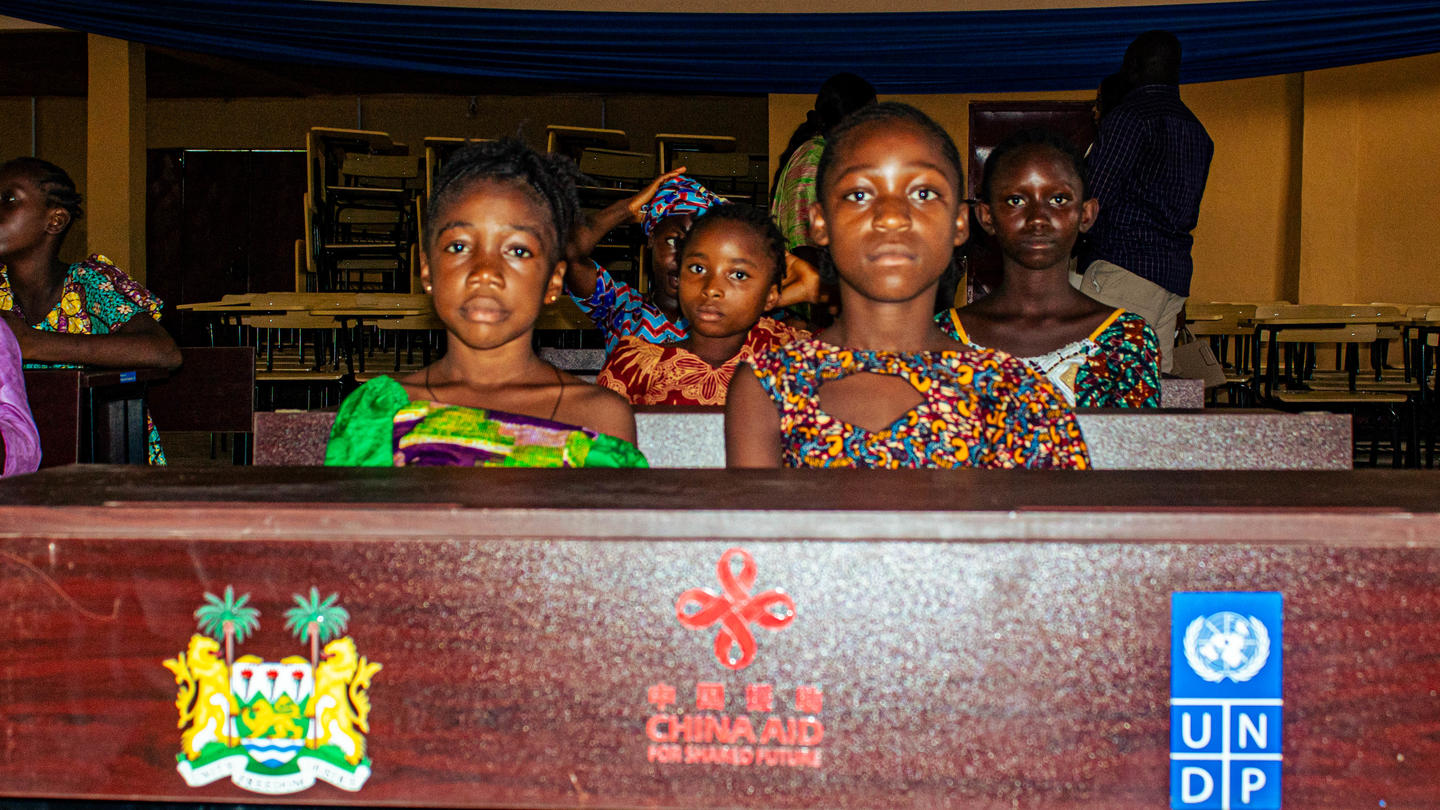 Group of women seated behind a banner featuring a crest and the UNDP logo.