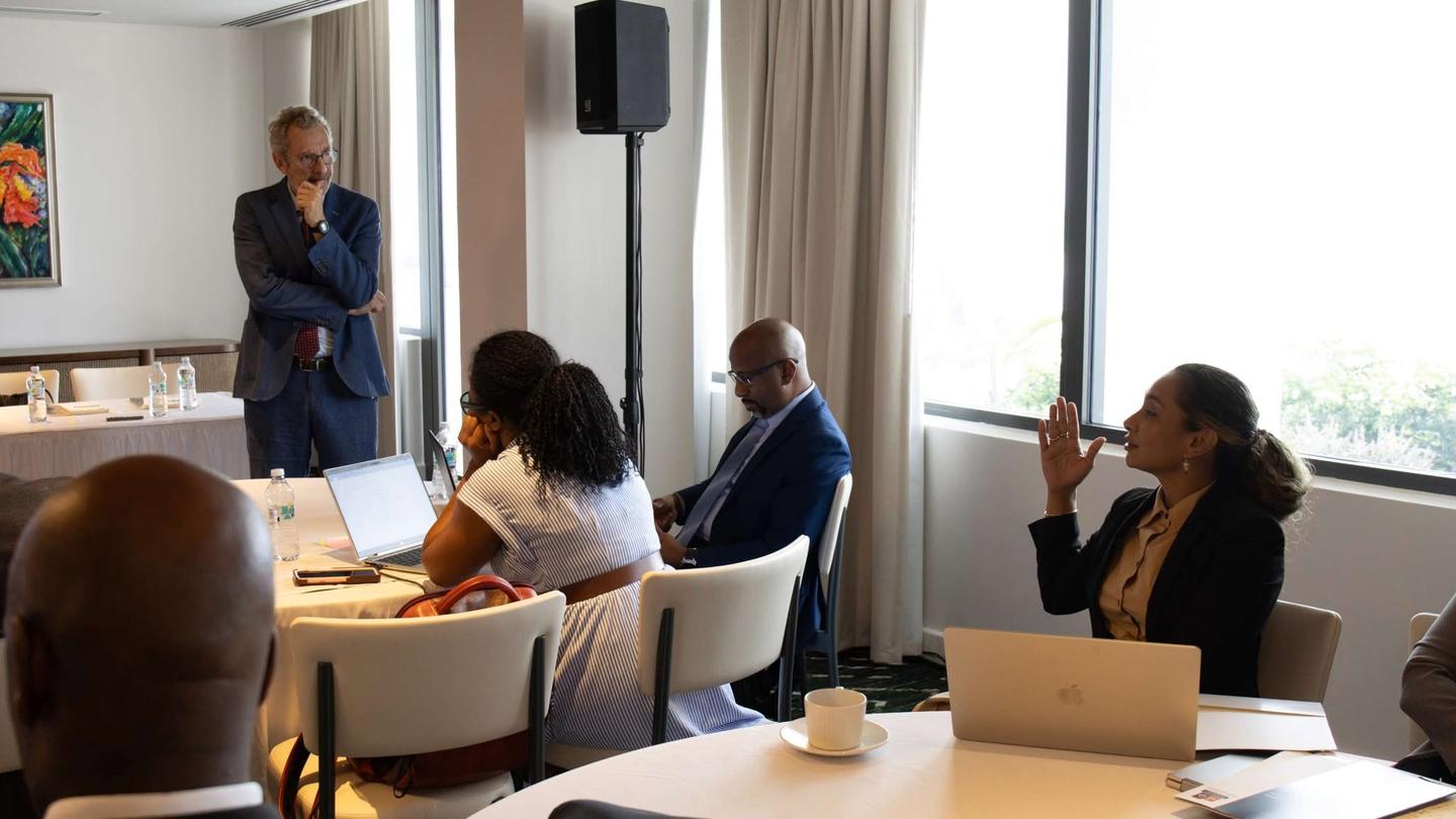 Bright conference room; presenter at the front, attendees around a table.