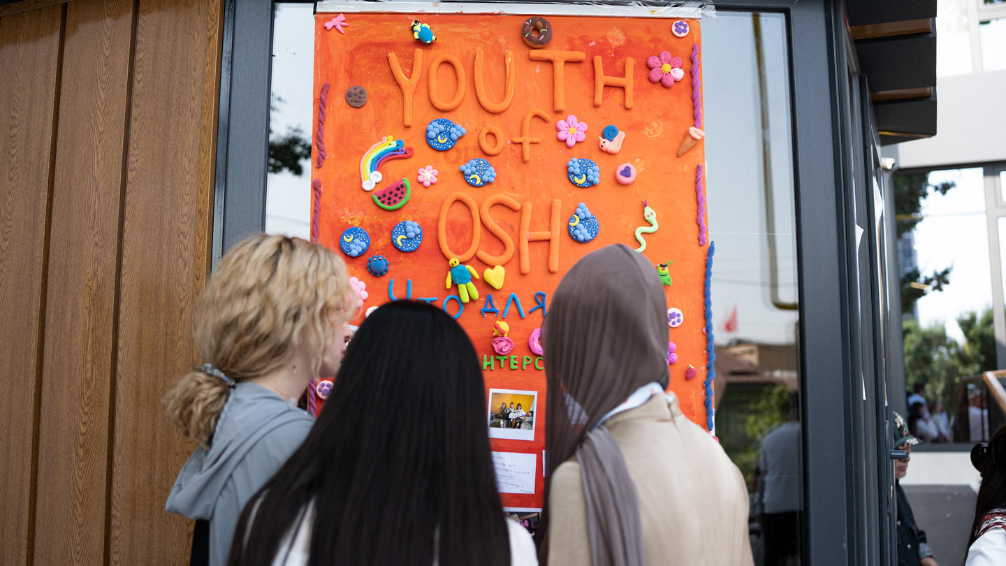 Three people with backs to camera looking at an orange poster with donut illustrations on a storefront window.