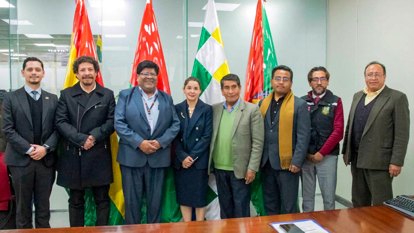 Group of people in a conference room posing for a photo with flags behind.