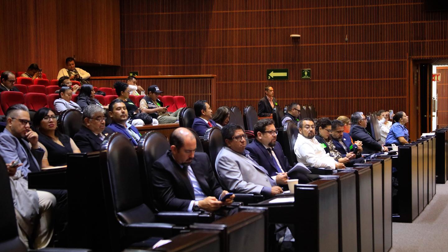 Audience in a wood-paneled conference hall listening to a presentation.