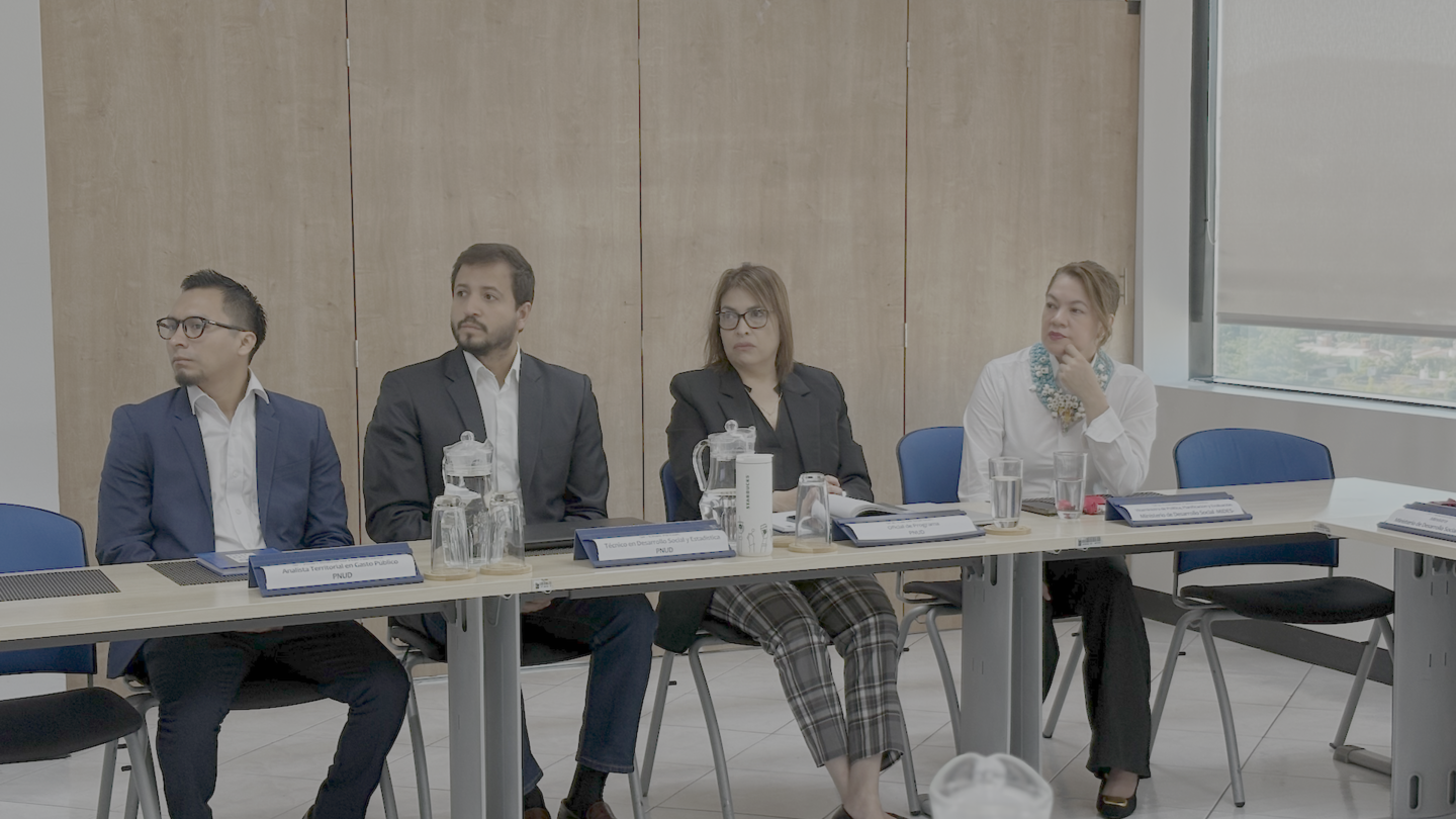 Five professionals at a conference table in a wood-paneled meeting room.