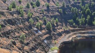 Steep rocky terrain with sparse trees surrounding a dark water-filled pit.