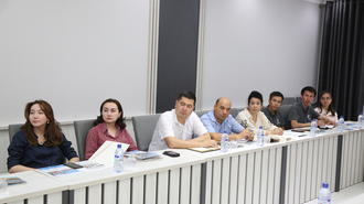 A group of eight people seated at a conference table, engaged in discussion.