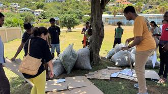 Group of people in a park participating in a cleanup, with trash bags piled near a tree.