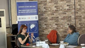 Panel discussion with three people seated at a table in front of a brick wall.