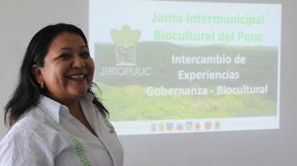 Presenter in white shirt beside a projected green slide on intermunicipal governance.