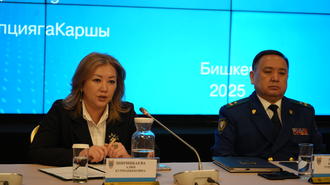 Photograph of two panelists at a conference table on a blue stage; one in a suit, one in a uniform.