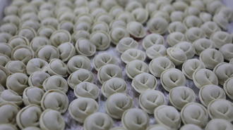 Close-up of numerous steamed dumplings with pleated edges arranged in rows.