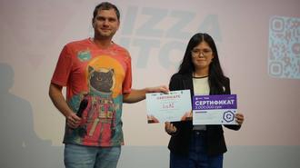 Two people on a stage holding certificates, a man in a red graphic T-shirt and a woman in dark clothing.