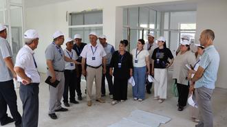 Group of people in white lab coats gather in a bright room, listening to a speaker.