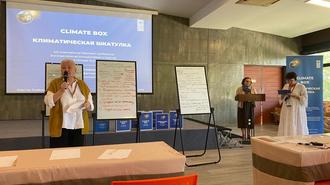 Two masked presenters lead a climate workshop in a classroom with a projector screen.