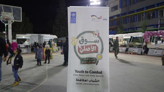 Nighttime outdoor basketball court with a white banner displaying Arabic text; people in background.