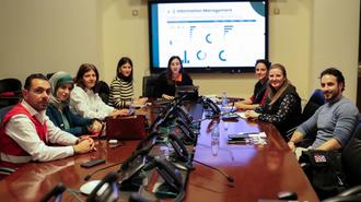 Group of people around a conference table in a meeting room with a presentation on screen.