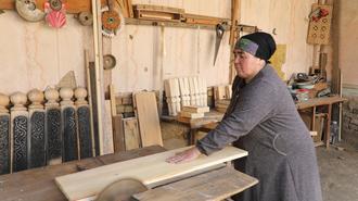 Photograph of a woman wearing a dark hat planing a board in a rustic woodshop.