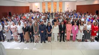 Large diverse group on stage posing for a group photo in a conference hall.