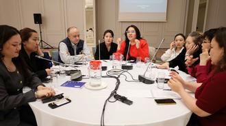Diverse group of professionals around a round table in a conference room; microphones on the table.