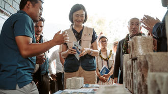 Outdoor booth with a group around a table; smiling woman in center shows a brochure.