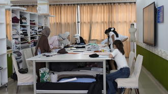 Photograph: Group of students in a sewing class around a table with fabric and tools.