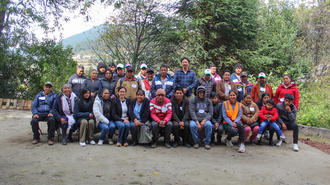 Group of people posing for a photo in an outdoor park with trees in the background.