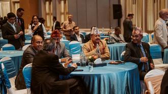 Attendees in formal attire sit around round tables with blue tablecloths in a banquet hall.