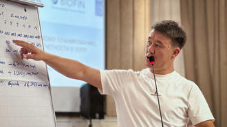 Man in a white shirt points at a flip chart during a presentation.