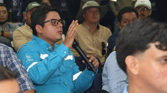 Audience member in blue shirt and glasses raises his hand at a conference.