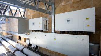 Photo: Industrial electrical control panels mounted on brick wall with pipes and steel framework.
