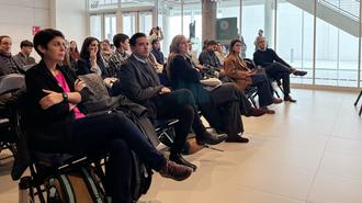Photograph of a diverse audience seated in rows in a bright conference room.