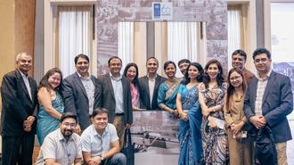 Group of diverse people posing for a photo indoors, some in traditional Indian and formal attire.