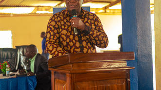 Man in a colorful patterned shirt speaks at a wooden podium with a microphone.