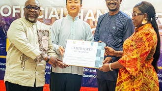 Five people on stage during a certificate award ceremony; center man receives a certificate.