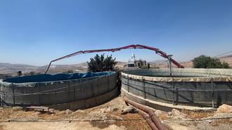 Photograph of two circular concrete water tanks with a red arch over them in a desert landscape.