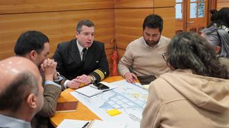 Group of people around a table with a large map and yellow sticky notes in a wood-paneled room.