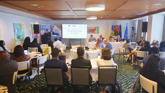 Conference attendees seated around tables in a meeting room watching a projector screen.