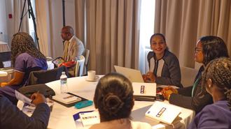 Group of people around a round table in a conference room, smiling, with papers and laptops.