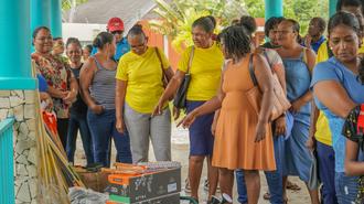 Photograph of a crowd at an outdoor market beside blue pillars; man in yellow shirt among shoppers.