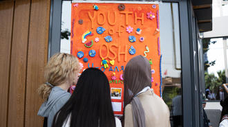 Three people with backs to camera looking at an orange poster with donut illustrations on a storefront window.