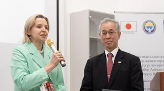 Photo: Woman in mint blazer speaks into microphone beside man in suit at a conference.