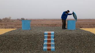 Two people in blue jackets atop a gravel mound, arranging blue blocks and a striped path.
