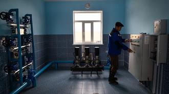 Technician in blue coveralls examines an electrical panel in a blue-walled workshop.