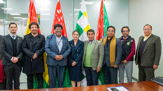 Group of people in a conference room posing for a photo with flags behind.