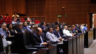 Audience in a wood-paneled conference hall listening to a presentation.